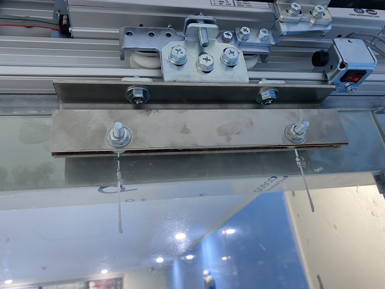 Cụm ray trượt cửa kính tự động với kẹp kính và bu lông siết chặt trên thanh nhôm